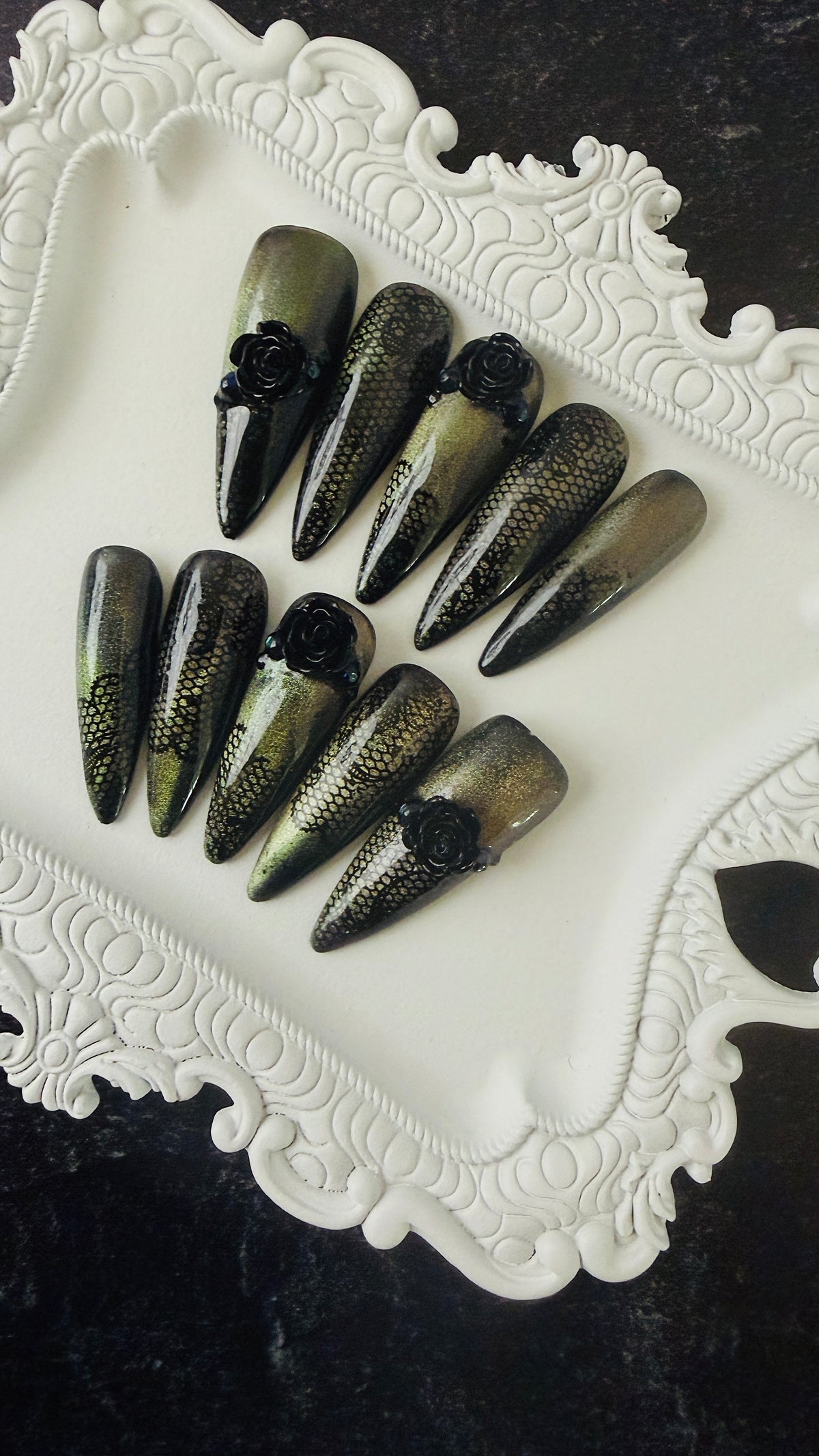 Black-and-gold stiletto press-on nails with lace detailing and sculpted black roses.